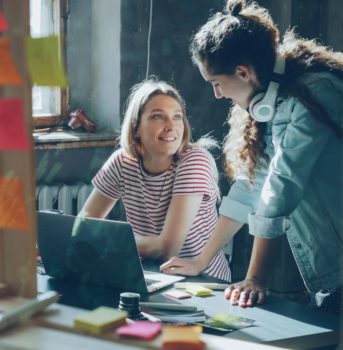 Two women collaborate over a laptop in an office.